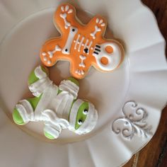 two decorated cookies sitting on top of a white plate next to an orange and green cookie