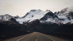 an empty road with snow covered mountains in the backgrounnd, near canmore