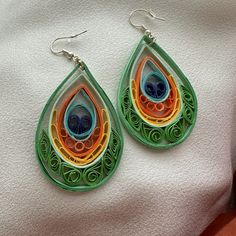 a pair of earrings made out of paper on top of a white cloth covered surface