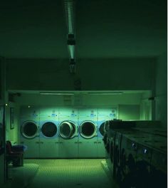 a row of washers in a dark room with green lights on the walls and floor