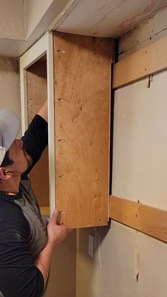 a man wearing a cowboy hat and working on a cabinet in a room with unfinished walls