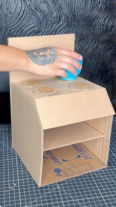 a person's hand on top of a cardboard box with a mouse in it