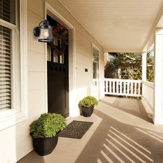 two planters on the front porch of a house with white siding and black doors