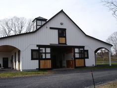 a large white barn with black trim on the front and side windows, along with an arched doorway