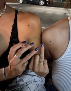 two women with blue and white nail polishes on their hands, one holding a cell phone