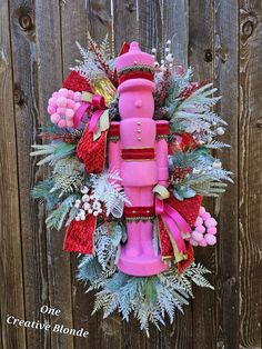 a wreath made out of pink and red items on a wooden fence with the words, one creative blond