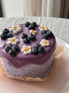 a purple cake with blueberries and white flowers on it sitting on top of a plate