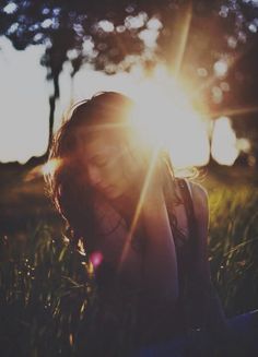 a woman is sitting in the grass with the sun shining through her hair and eyes