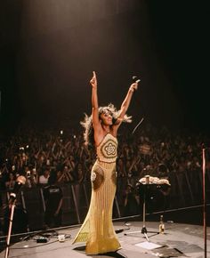 a woman is dancing on stage with her arms in the air as she sings to an audience