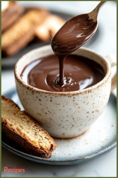 chocolate sauce being poured into a white bowl on a plate with bread and crackers in the background