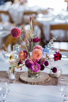 a vase filled with lots of flowers on top of a table next to wine glasses