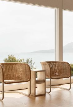 two chairs sitting next to each other in front of a large window with the ocean outside