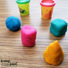 five different colored play doughs on a wooden table