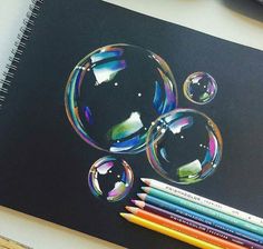 a spiral notebook with colored pencils next to it and an image of two soap bubbles