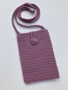 a crocheted bag is shown on a white surface with a purple cord attached to it