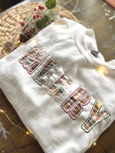 a white shirt with the word happy on it sitting next to a basket and christmas lights