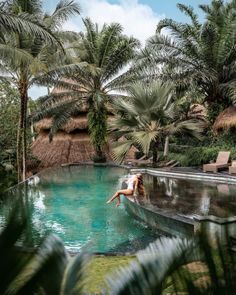 a woman sitting on the edge of a swimming pool surrounded by palm trees