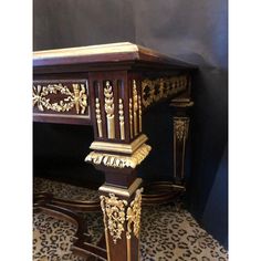 an ornate wooden table with gold decorations on it's legs and top, against a black wall