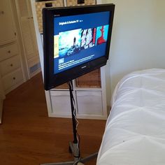 a flat screen tv sitting on top of a wooden floor next to a white bed