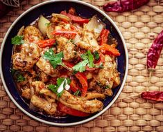 a bowl filled with chicken and vegetables on top of a woven table cloth next to red peppers