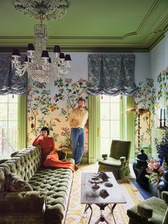 a man and woman standing in a living room with floral wallpaper on the walls