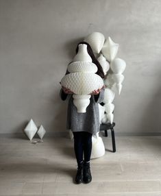 a woman standing next to a pile of white vases