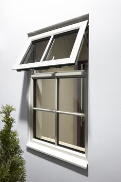 an open window on the side of a white wall next to a potted plant