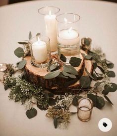 candles and greenery are arranged on top of a wooden slice that is sitting on a table