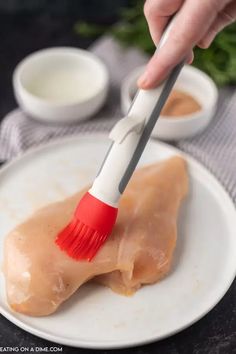 a person is using a brush to paint a piece of meat on a white plate