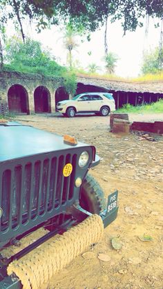 two jeeps parked in front of a building with trees and dirt on the ground