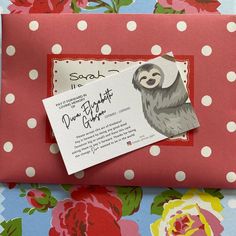 a card with a sloth on it sitting next to a red envelope and pink flowers