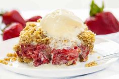 a piece of strawberry crumb pie on a plate with ice cream and strawberries in the background