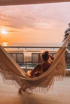 a woman sitting in a hammock looking out at the ocean