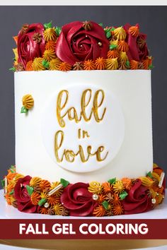 a white cake with red and orange flowers on it that says fall in love, surrounded by gold lettering