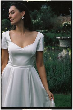 a woman in a white dress is walking through the grass with her hand on her hip