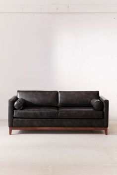 a black leather couch sitting on top of a white floor next to a wooden frame