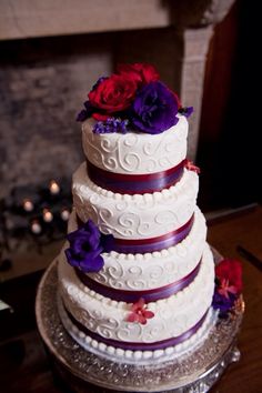 a wedding cake with purple and red flowers on it