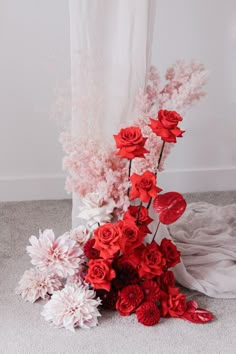 red and white flowers on the floor in front of a drapeed window with curtains