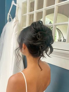 a woman standing in front of a window next to a wedding dress on a hanger