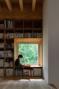 a person sitting at a window sill in front of a book shelf filled with books