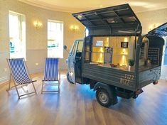 a small truck is parked in the middle of a room with blue chairs and windows