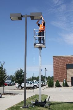 a man in an orange shirt is standing on a light pole with his hands up