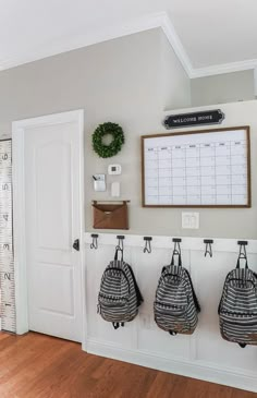 three backpacks hanging on hooks in front of a wall with a calendar and ruler