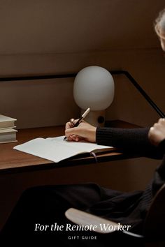 a person sitting at a desk writing on a piece of paper with a lamp in the background