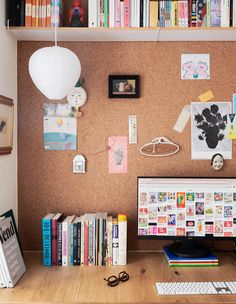 a desk with a computer, books and other items on top of the desk in front of a corkboard wall