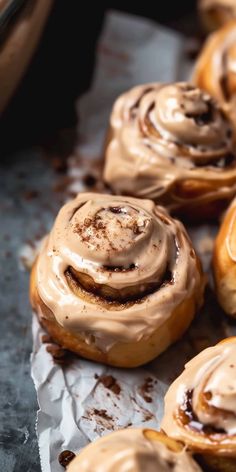 cinnamon rolls with frosting on top sitting on wax paper