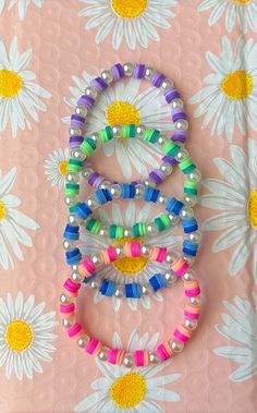 three bracelets are arranged on top of a flowered surface with daisies in the background