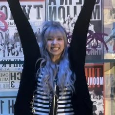 a woman standing in front of a wall with posters on it's sides and her arms up