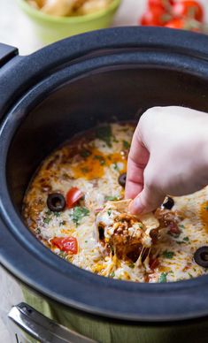 a person is dipping some food into a crock pot filled with cheese and olives