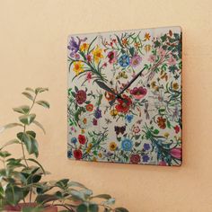 a clock that is on the side of a wall with flowers and plants around it